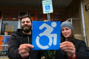 Brian Glenney and Sara Hendren holding the new wheelchair sign in front of the old one